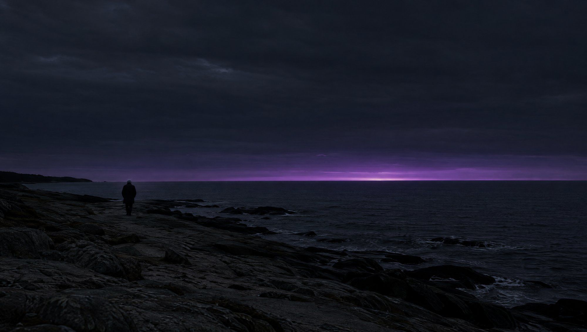A lone figure seen from far behind, walking along a dark rocky shoreline at dusk under a band of violet light on the horizon.